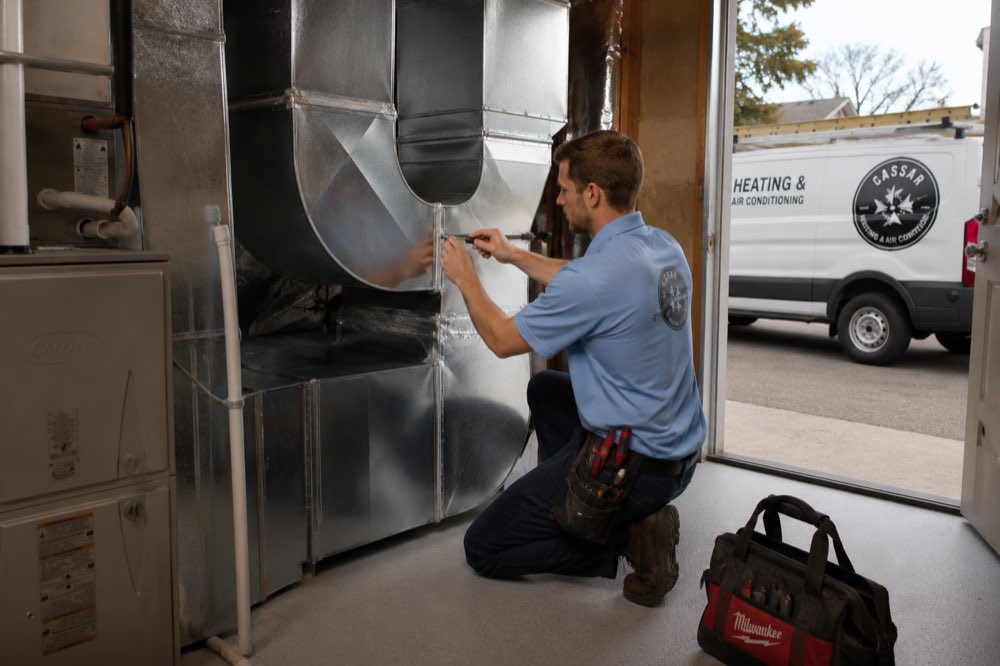 Cassar HVAC technician fitting sheet metal ductwork at the furnace plenum in Whitby, Ontario
